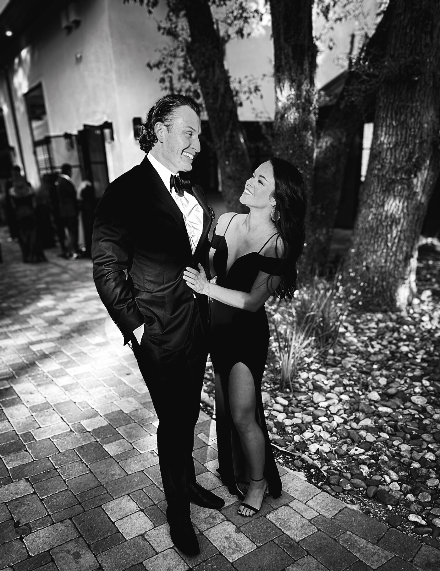 Sean in a black tuxedo and Brittany in a black gown, smiling at each other beneath the trees
