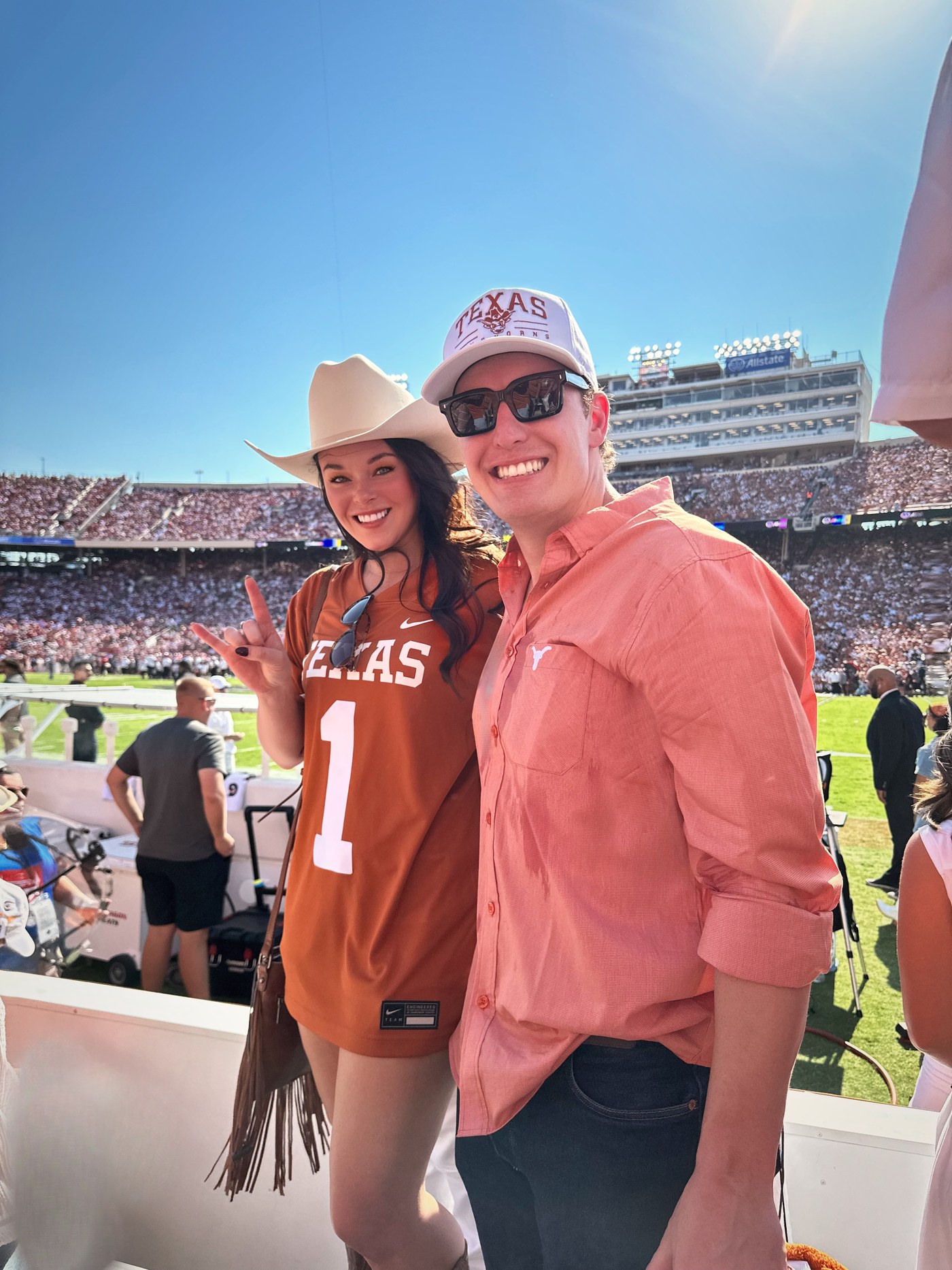 Brittany in a Texas jersey and cowboy hat flashing the Hook 'em sign beside Sean at a packed football stadium